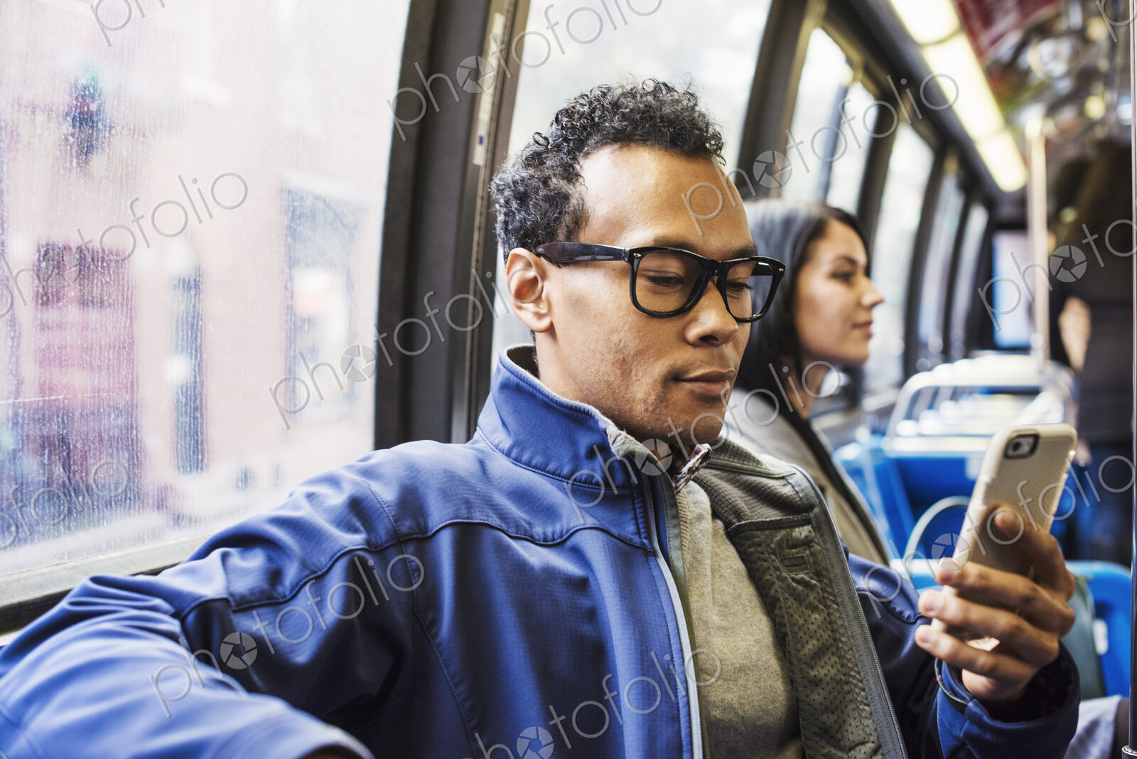 A young man and a young woman sitting on public transport looking at their cellphones.