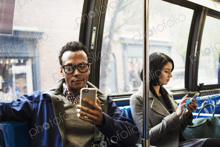 A young man and a young woman sitting on public transport looking at their cellphones.