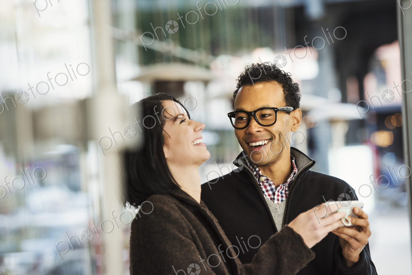 A young man and woman holding a cellphone together and laughing.