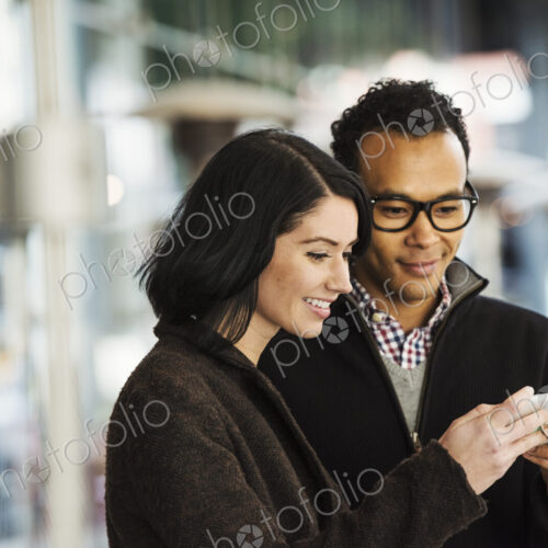 A young man and woman holding a cellphone together and looking at the screen. A young man and woman holding a cellphone together and looking at the screen.