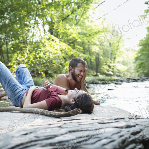 A young man and woman lying on the rocks on a river bank. A young man and woman lying on the rocks on a river bank.