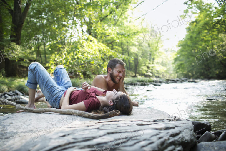 A young man and woman lying on the rocks on a river bank.
