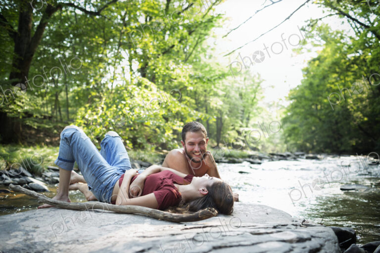 A young man and woman lying on the rocks on a river bank.
