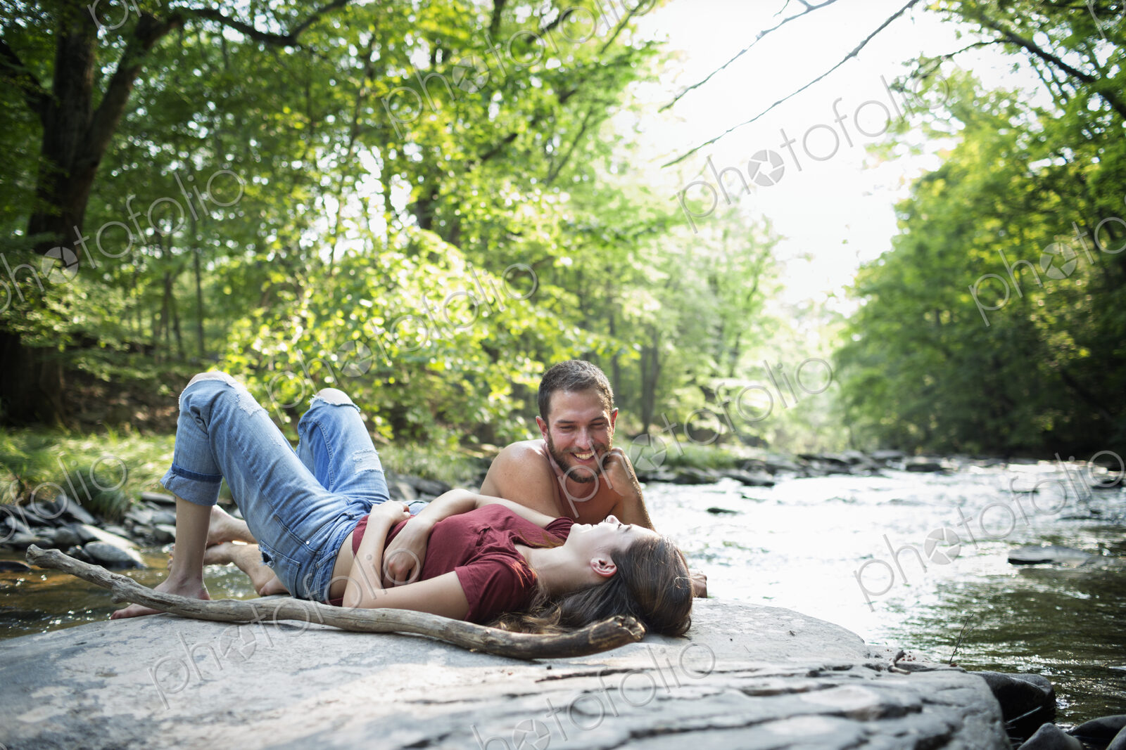 A young man and woman lying on the rocks on a river bank.