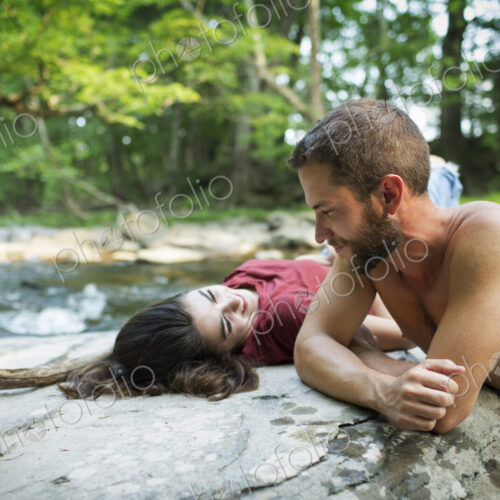 A young man and woman lying on the rocks on a river bank. A young man and woman lying on the rocks on a river bank.