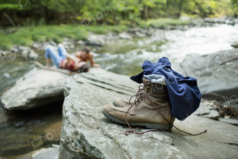 A young man and woman on the rocks on a river bank. Jeans and boots on a rock.