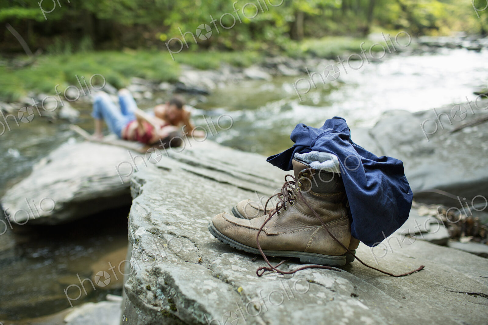 A young man and woman on the rocks on a river bank. Jeans and boots on a rock.
