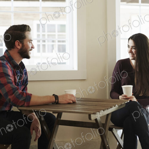 A young man and woman sitting at a table holding paper cups. A young man and woman sitting at a table holding paper cups.