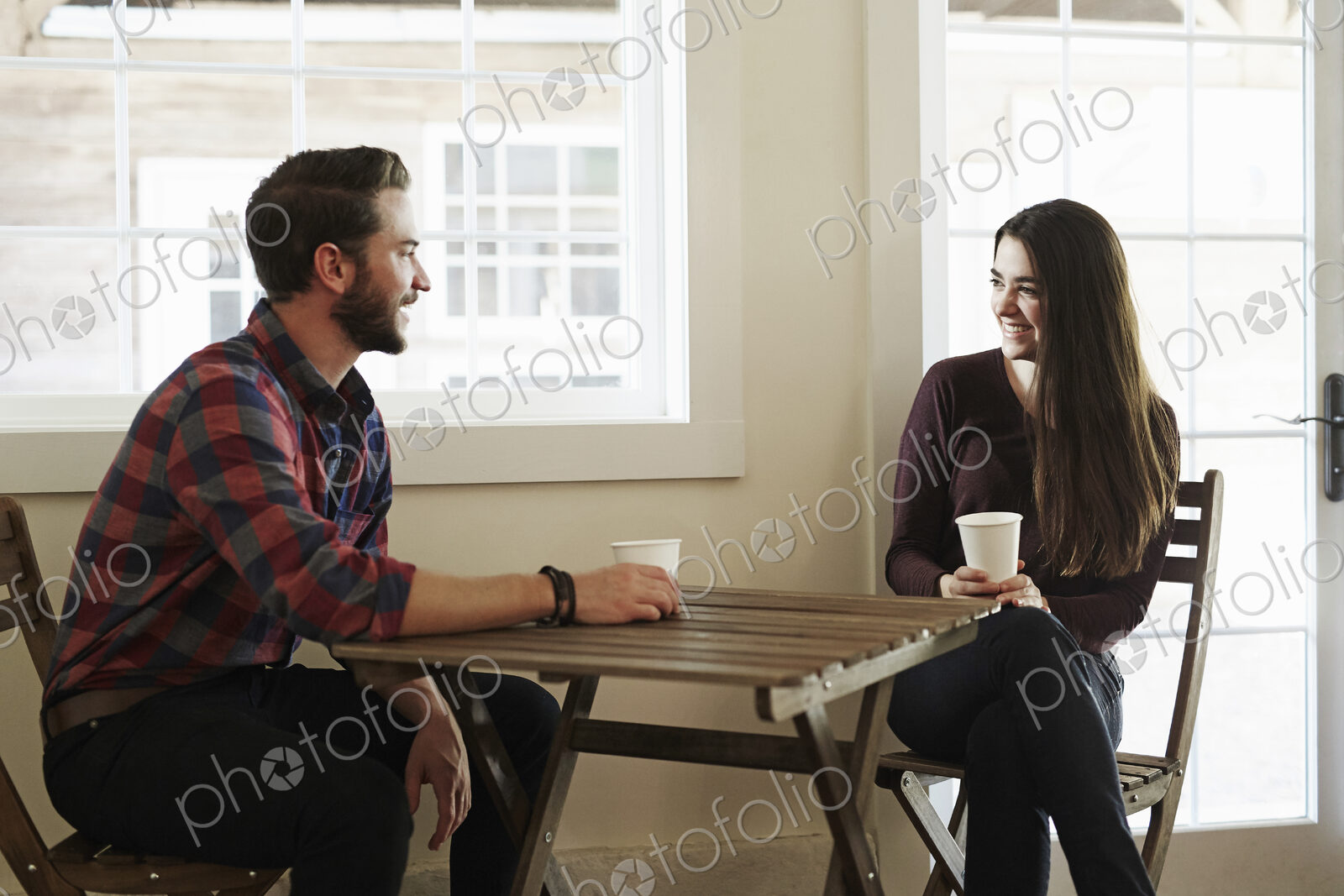 A young man and woman sitting at a table holding paper cups.