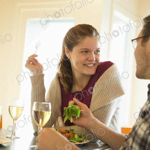 A young man and woman sitting together having a meal and drinking wine.