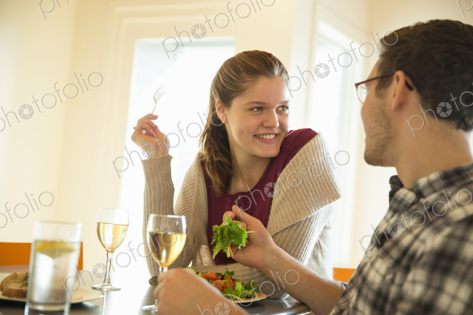 A young man and woman sitting together having a meal and drinking wine.
