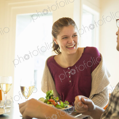 A young man and woman sitting together having a meal and drinking wine.