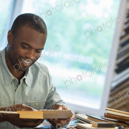 A young man at his workbench in a picture framing studio. Surrounded by samples.