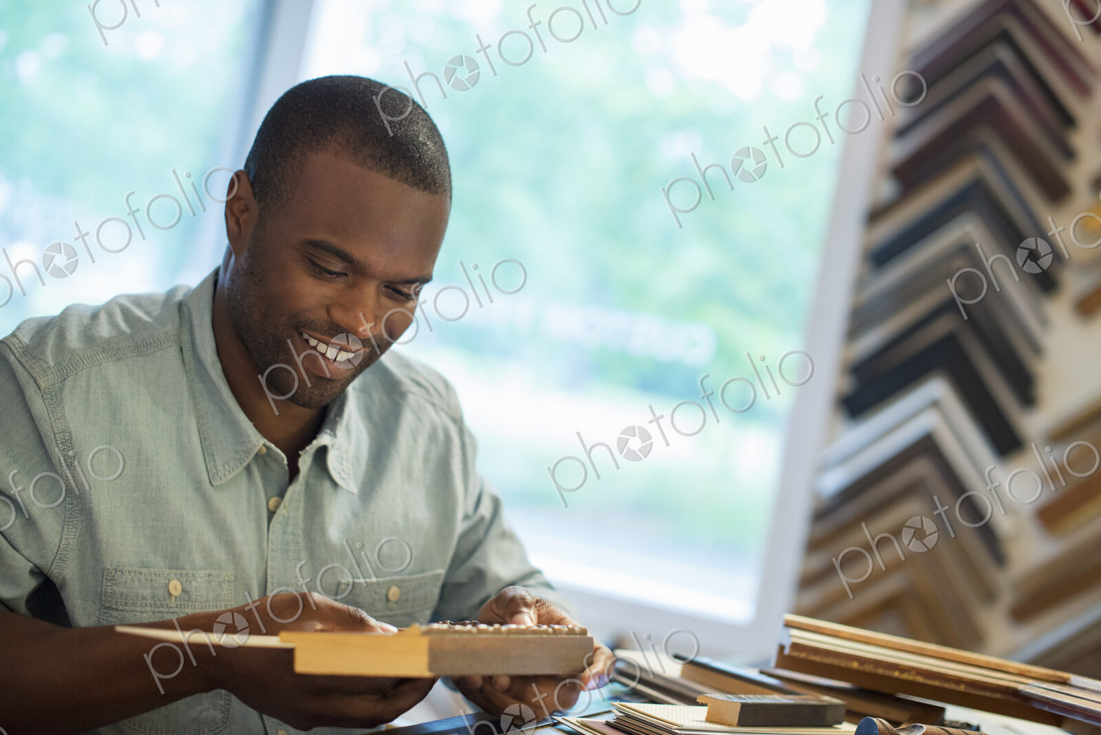 A young man at his workbench in a picture framing studio. Surrounded by samples.