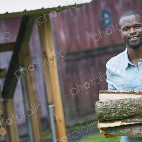 A young man carrying a pile of logs in from the logstore. Farm life.