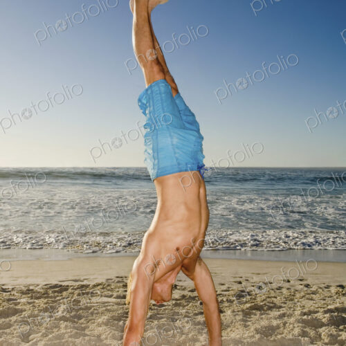 A young man doing a handstand on the sand in Cape Town.