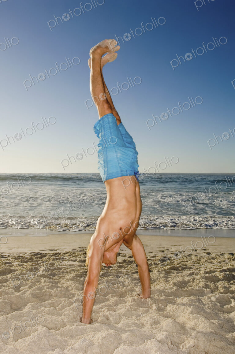 A young man doing a handstand on the sand in Cape Town.