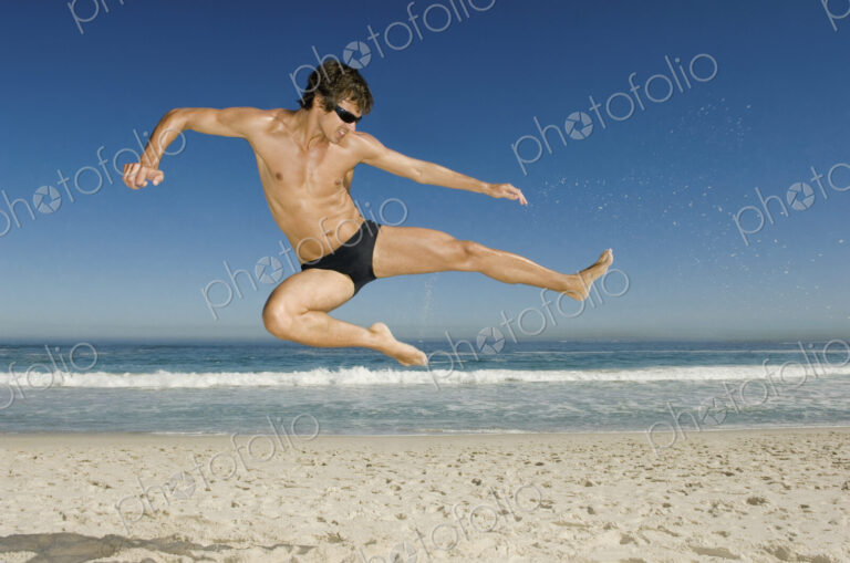 A young man doing a karate style leap on the beach in Cape Town.