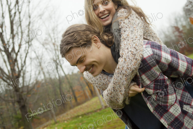 A young man giving a woman a piggyback. An organic farm setting.