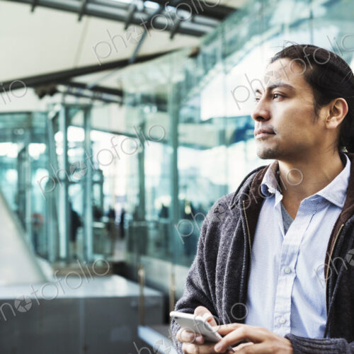 A young man holding his mobile phone, standing on a busy walkway. A young man holding his mobile phone, standing on a busy walkway.