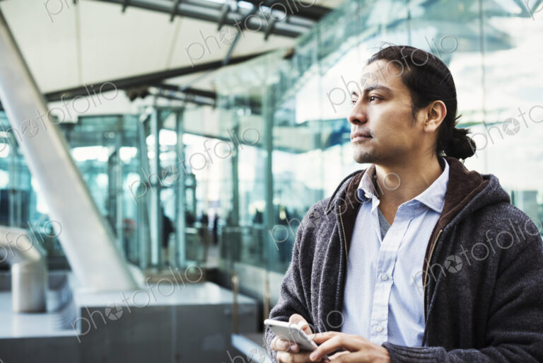 A young man holding his mobile phone, standing on a busy walkway.