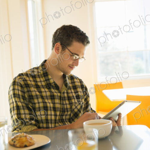 A young man in a coffee shop reading using a tablet computer.