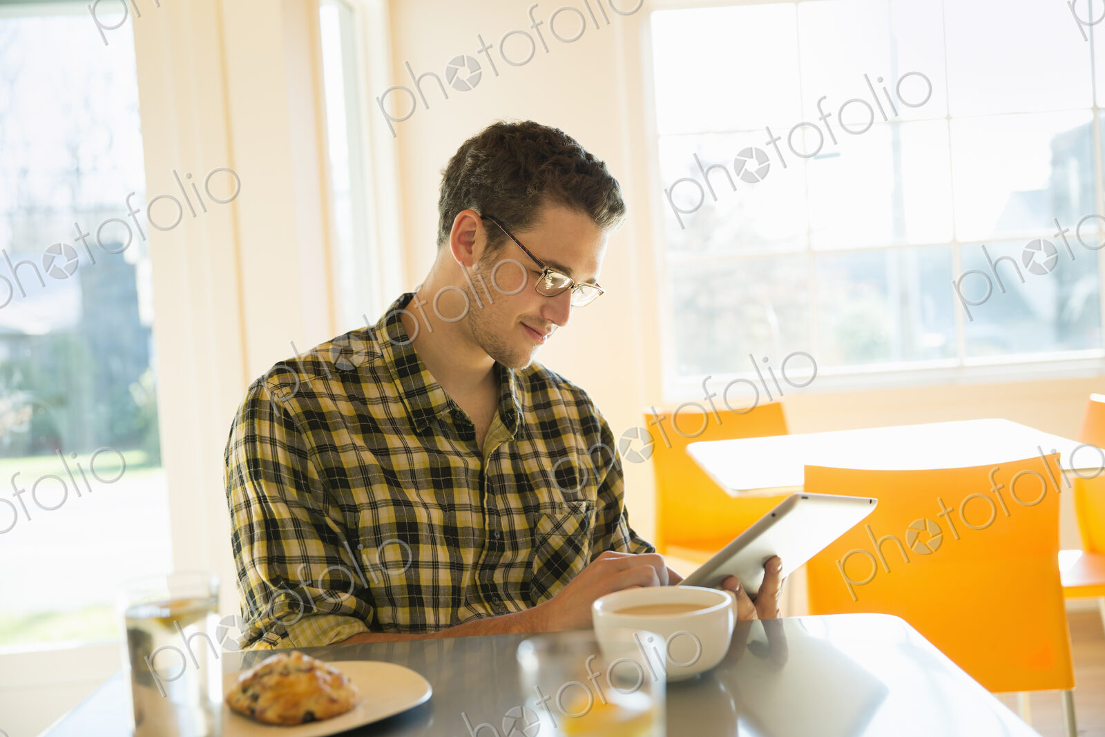A young man in a coffee shop reading using a tablet computer.