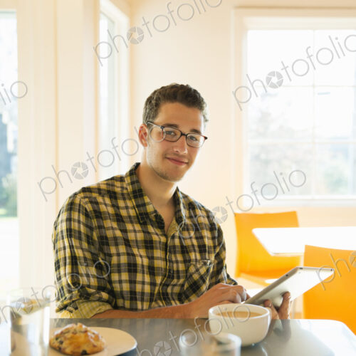 A young man in a coffee shop reading using a tablet computer.