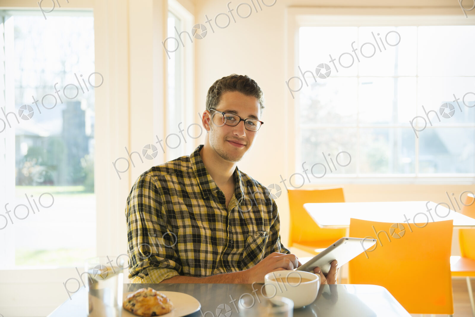 A young man in a coffee shop reading using a tablet computer.