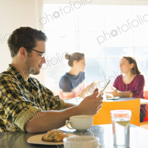 A young man in a coffee shop reading using a tablet computer.