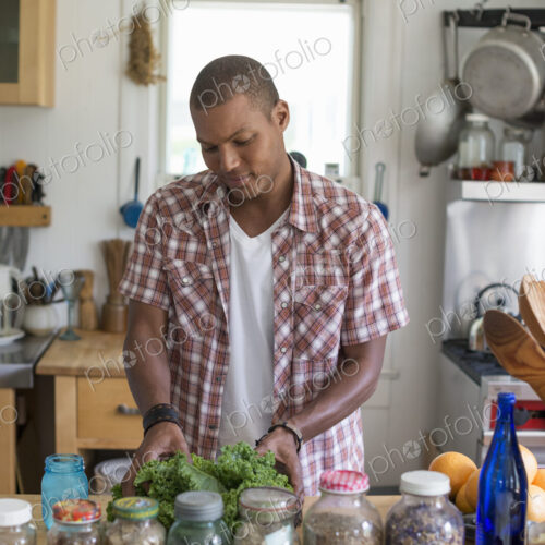 A young man in a kitchen preparing salad leaves and vegetables.