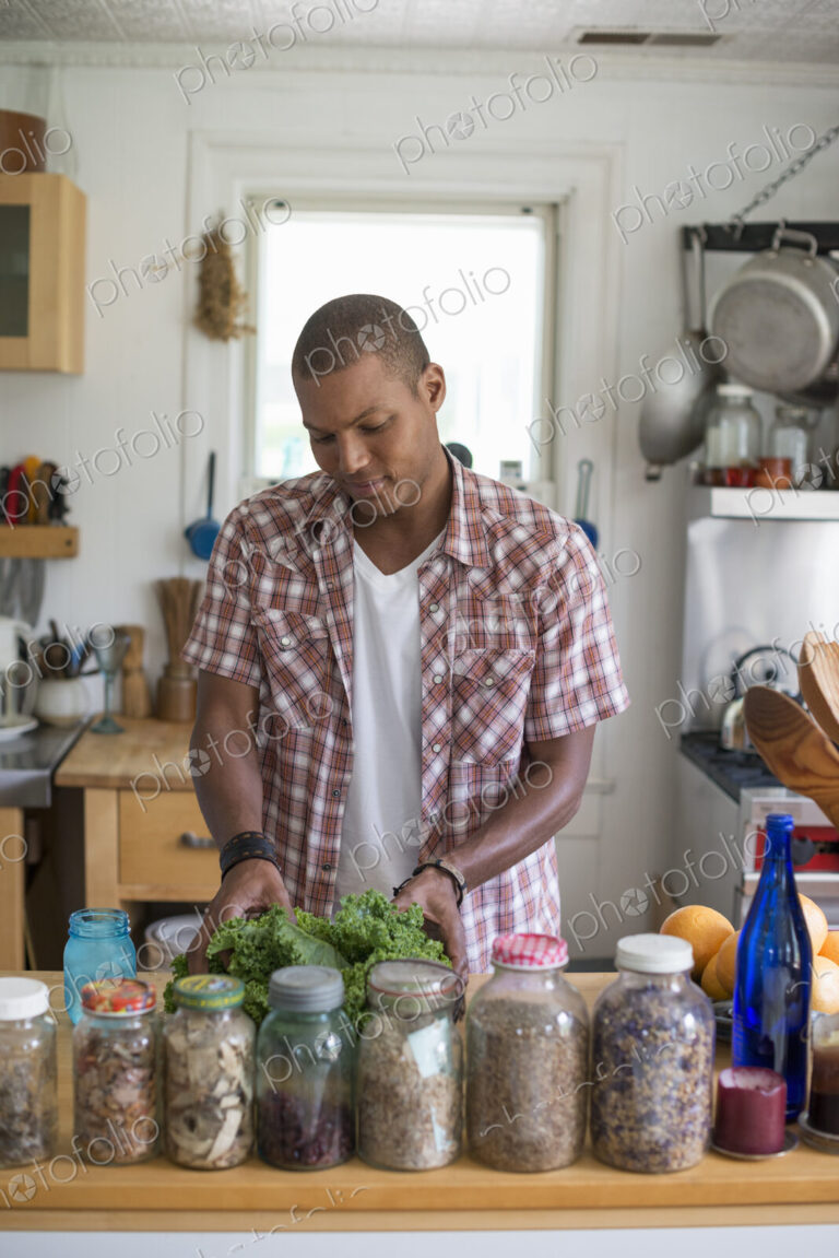 A young man in a kitchen preparing salad leaves and vegetables.