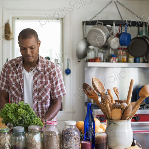 A young man in a kitchen preparing salad leaves and vegetables.