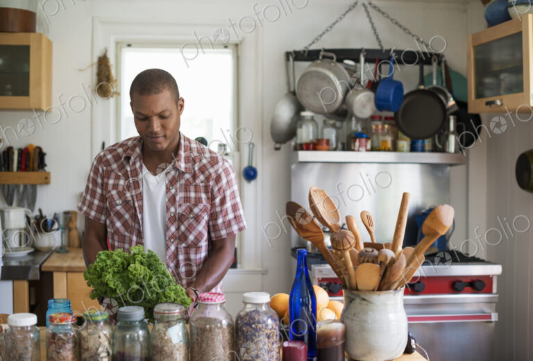 A young man in a kitchen preparing salad leaves and vegetables.