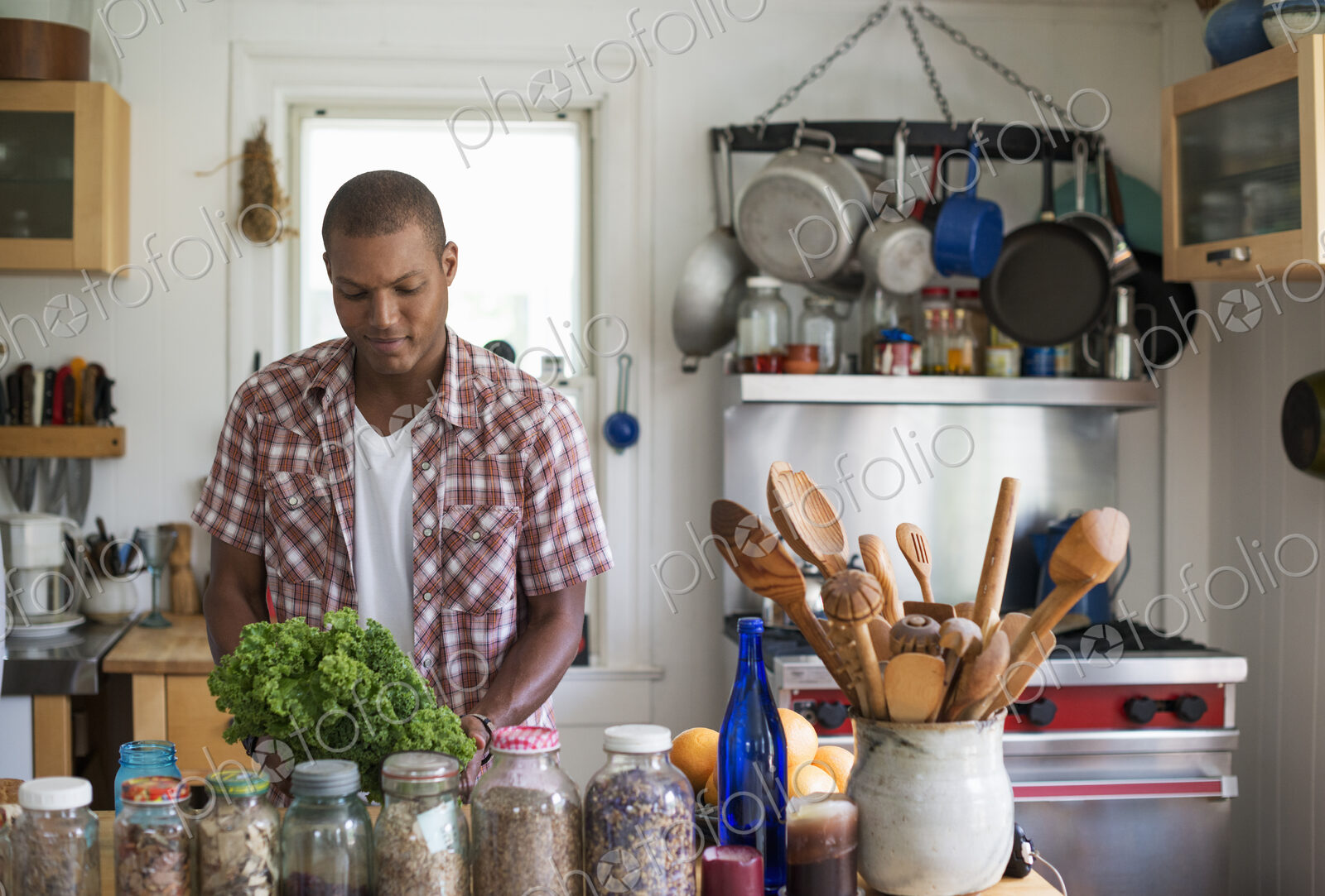 A young man in a kitchen preparing salad leaves and vegetables.