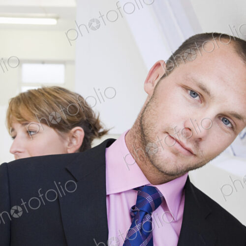 A young man in a suit and pink shirt, leaning against a wall, and a young woman in the… A young man in a suit and pink shirt, leaning against a wall, and a young woman in the…