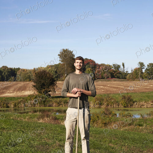 A young man in working clothes standing in a field, holding a tool. A young man in working clothes standing in a field, holding a tool.