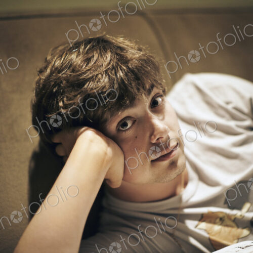 A young man lying on a sofa, resting his head on his elbow and looking at the camera. A young man lying on a sofa, resting his head on his elbow and looking at the camera.