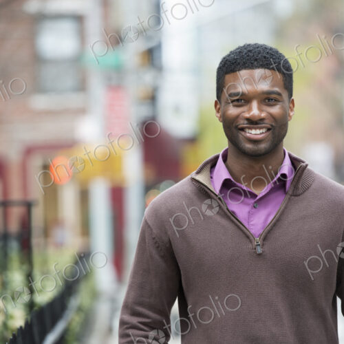 A young man outdoors on a street smiling.