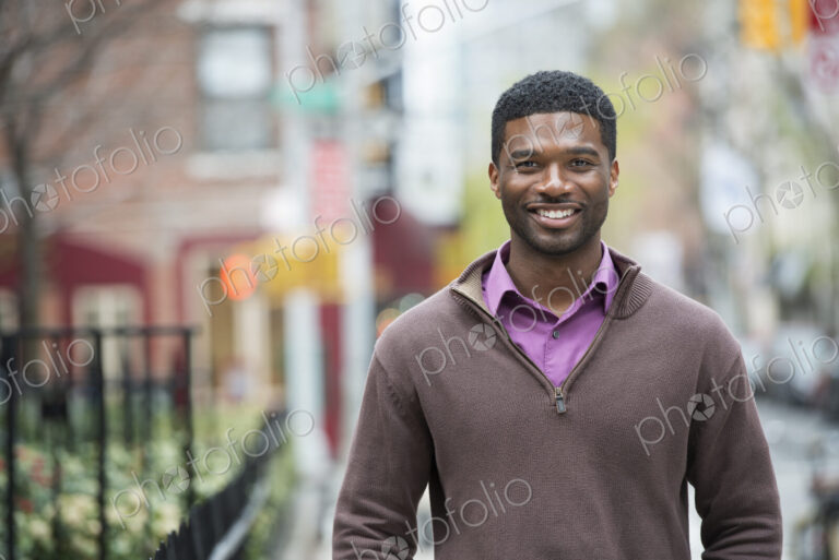 A young man outdoors on a street smiling.