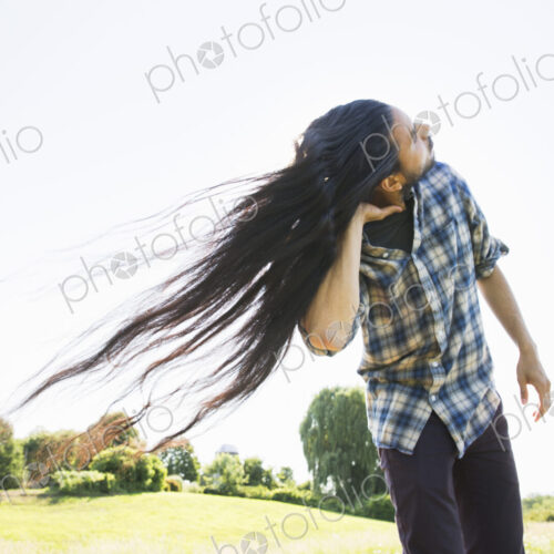 A young man shaking his head with his long hair flowing in the breeze.