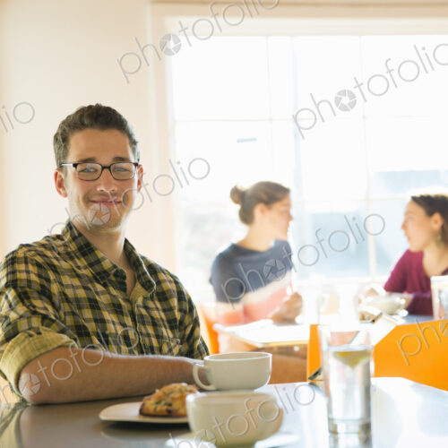 A young man sitting at a coffee shop counter, with two women in the background. A young man sitting at a coffee shop counter, with two women in the background.