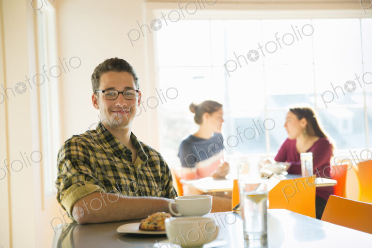 A young man sitting at a coffee shop counter, with two women in the background.