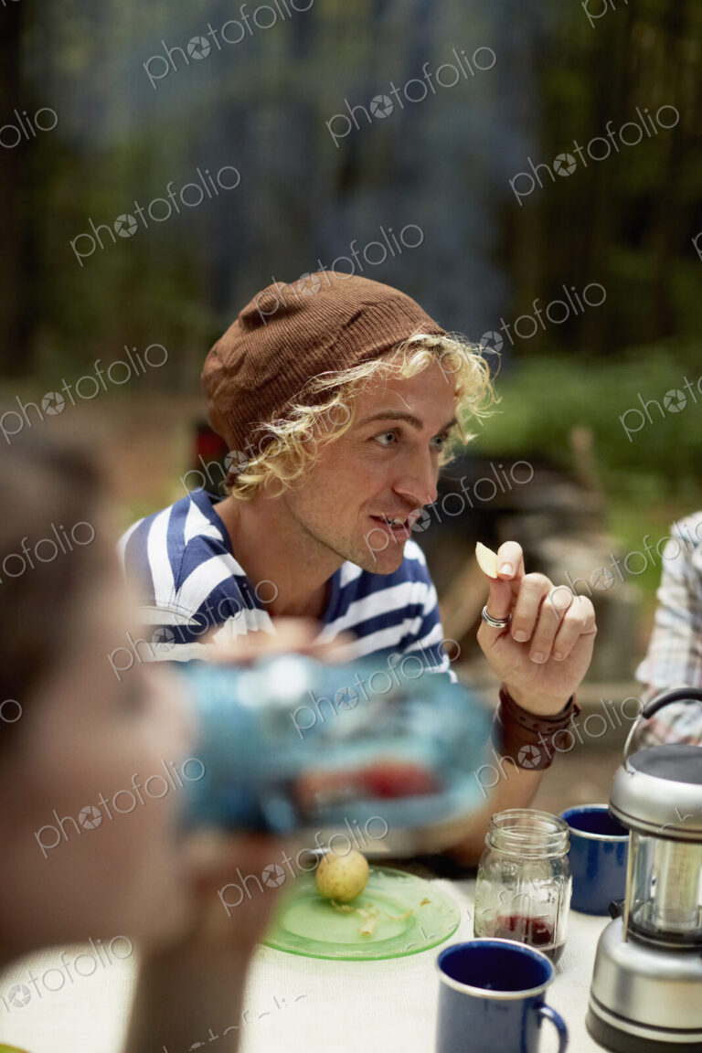 A young man sitting at a picnic table in the woods.