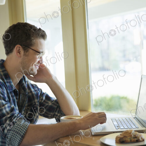 A young man sitting at a table using a laptop computer. A young man sitting at a table using a laptop computer.