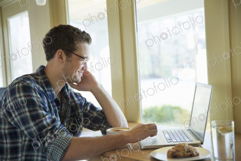 A young man sitting at a table using a laptop computer.