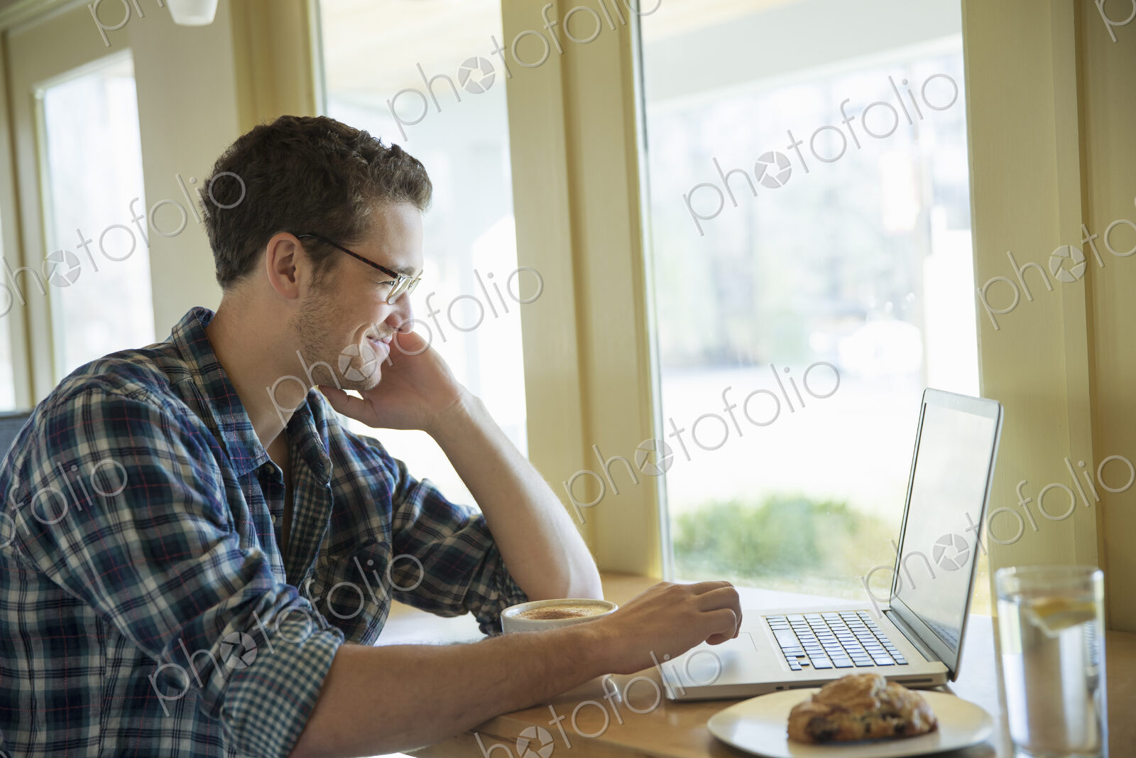 A young man sitting at a table using a laptop computer.