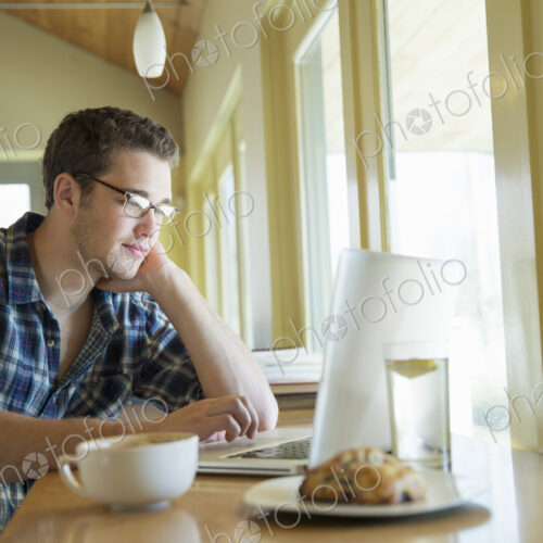 A young man sitting at a table using a laptop computer. A young man sitting at a table using a laptop computer.