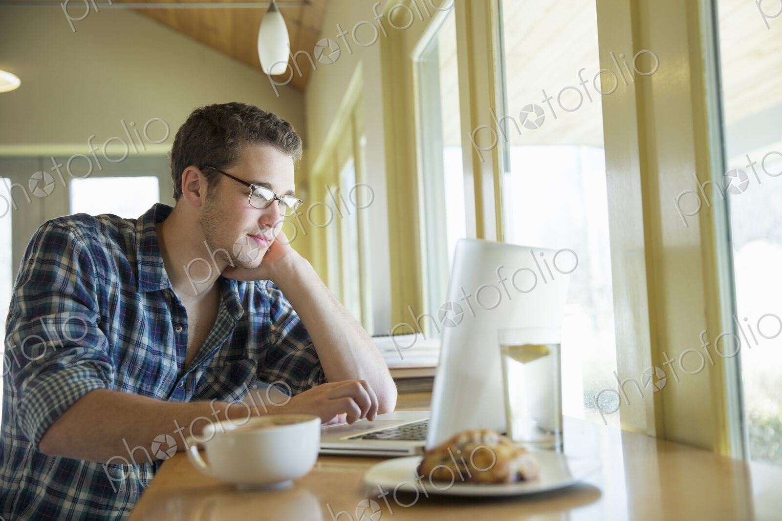 A young man sitting at a table using a laptop computer.