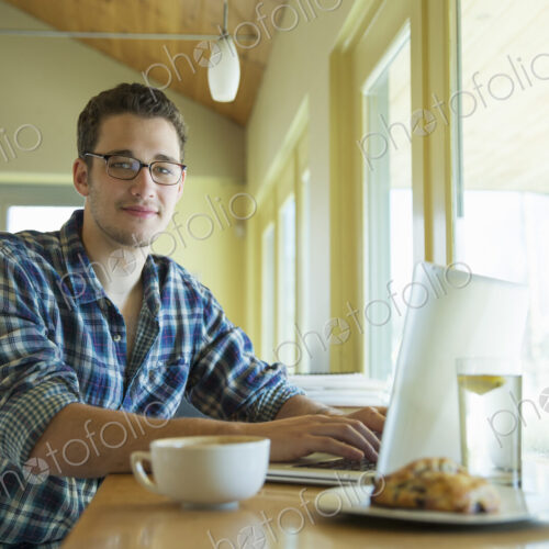 A young man sitting at a table using a laptop computer. A young man sitting at a table using a laptop computer.
